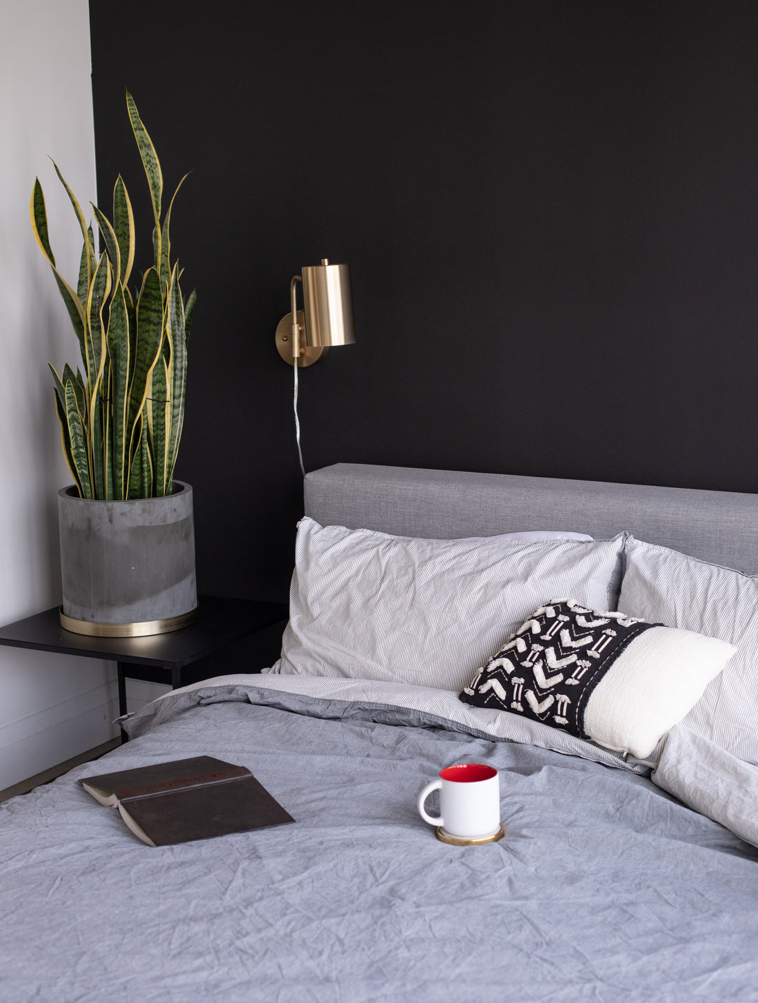 a cozy made bed with an open book and mug of tea on the bedspread. 